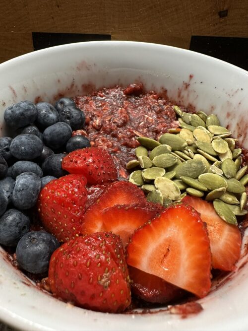Beet root oatmeal breakfast bowl with blueberries, strawberries, and pumpkin seeds in a white bowl — healthy, high-fiber, antioxidant-rich recipe.
